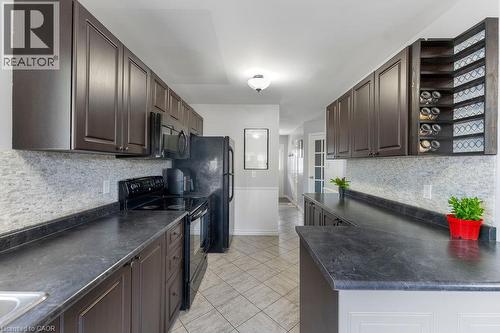 Galley kitchen featuring dark wood-finish cabinetry, black countertops, and a full tile backsplash - 33 Remple Court, Cambridge, ON - Indoor Photo Showing Kitchen