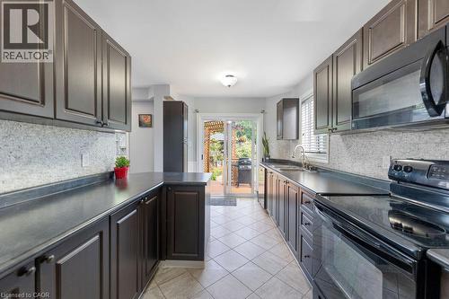 Galley kitchen featuring dark wood-finish cabinetry, light-toned tiled flooring, and a sliding glass door providing direct access to the outdoor space - 33 Remple Court, Cambridge, ON - Indoor Photo Showing Kitchen