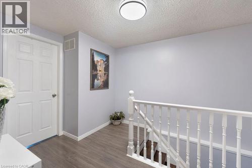 Upper landing featuring wood-finish flooring, white paneled door, and a staircase with white spindles and handrail - 33 Remple Court, Cambridge, ON - Indoor Photo Showing Other Room