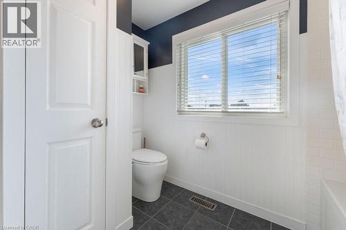 Bathroom featuring a white toilet, dark floor tiles, a window with horizontal blinds, wainscoting, and a wall-mounted storage cabinet - 33 Remple Court, Cambridge, ON - Indoor Photo Showing Bathroom