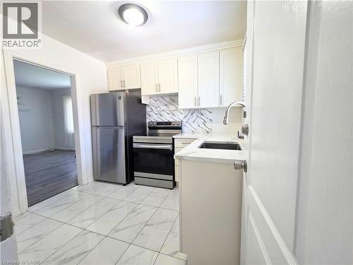 Modern kitchen featuring stainless steel appliances, white cabinetry with soft-close doors, geometric tile backsplash, quartz countertops, and an island with an undermount sink and chrome faucet - 353 East 21St Street, Hamilton, ON - Indoor Photo Showing Other Room
