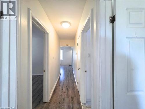 Bright hallway featuring warm ceiling lighting, wood-finish flooring throughout, and multiple white panel doors providing access to adjacent rooms - 353 East 21St Street, Hamilton, ON - Indoor Photo Showing Other Room