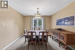 Recessed lighting and a decorative chandelier illuminate this room, featuring light tan walls, textured carpeting, and white baseboards - 