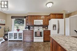 Kitchen featuring wood cabinetry, white appliances, a patterned backsplash, and wood-finish flooring - 