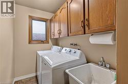 Dedicated laundry area featuring a utility sink with dual-handle faucet, wood-finish upper cabinetry, and a window with wood trim - 