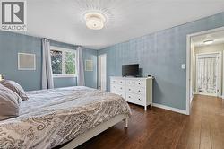 Bedroom featuring wood-finish flooring, a double window with light-colored drapes, and a decorative ceiling light fixture - 