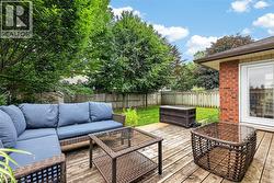 Expansive wood-finish deck with ample space for outdoor living, featuring a glass-paneled patio door, red brick exterior, and a fenced yard with mature trees - 