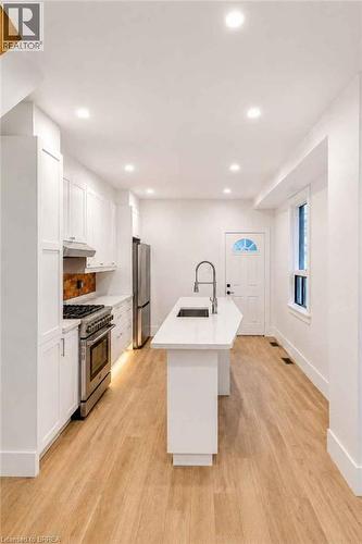 Recessed lighting illuminates the kitchen featuring white cabinetry, stainless steel appliances, a center island with an undermount sink, and wood-finish flooring - 561 Wentworth Street N, Hamilton, ON - Indoor Photo Showing Kitchen