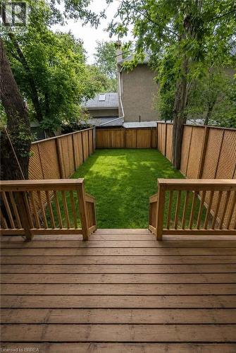 Wood-finish deck with railing leading to a private fenced backyard with a manicured lawn. AI used for backyard photo - 561 Wentworth Street N, Hamilton, ON - Outdoor With Deck Patio Veranda