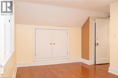 Wood-finish flooring, white trim, attic access panel with brass hardware, and a white interior door - 41 Paradise Road S, Hamilton, ON - Indoor Photo Showing Other Room