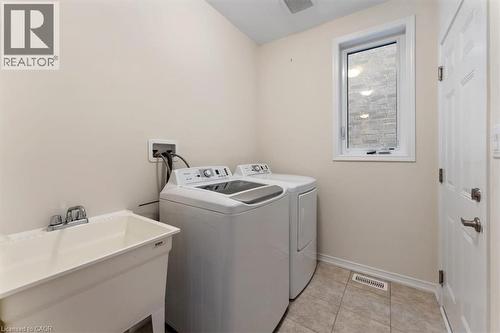 Clothes washing area with light tile patterned floors, washing machine and dryer, a sink, laundry area, and baseboards - 13 Steven Drive, Thorold, ON - Indoor Photo Showing Laundry Room