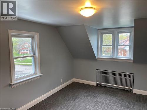 Sloped ceilings, two distinct windows, a flush-mount ceiling light fixture, and a floor-level radiator - 49 West Avenue, Kitchener, ON - Indoor Photo Showing Other Room