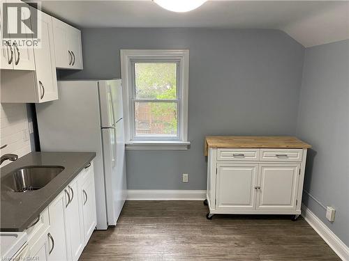 White cabinetry, stainless steel sink, wood-finish flooring, white appliances, and a window providing natural light - 49 West Avenue, Kitchener, ON - Indoor Photo Showing Kitchen