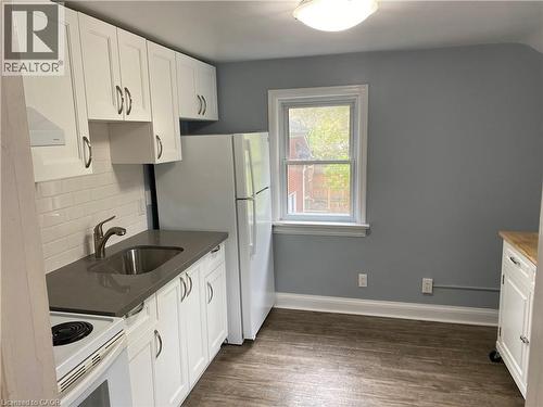 White shaker-style cabinetry, subway tile backsplash, solid surface countertops, stainless steel sink with a modern faucet, and wood-finish flooring - 49 West Avenue, Kitchener, ON - Indoor Photo Showing Kitchen
