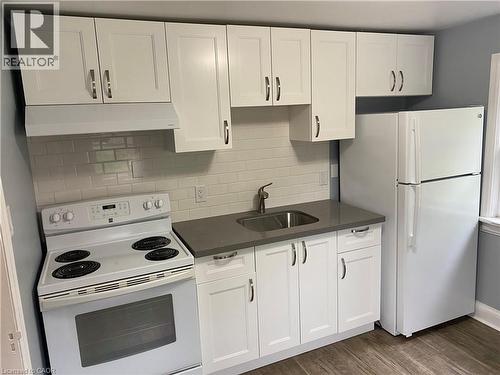 White cabinetry, subway tile backsplash, white electric range, stainless steel sink, and wood-finish flooring - 49 West Avenue, Kitchener, ON - Indoor Photo Showing Kitchen