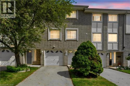 Grey brick exterior facade, two-car garage, multiple windows with venetian blinds, concrete driveways, and established landscaping - 145 Rice Avenue Unit# 2, Hamilton, ON - Outdoor With Facade