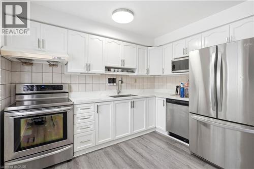 Kitchen featuring white cabinetry, stainless steel appliances, a tile backsplash, light countertops, and wood-finish flooring - 145 Rice Avenue Unit# 2, Hamilton, ON - Indoor Photo Showing Kitchen