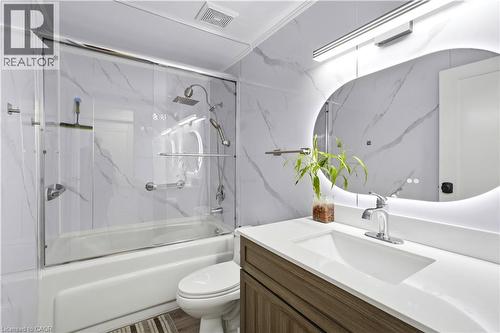 Contemporary bathroom featuring a tub and shower combination with a glass enclosure, a vanity with a white countertop and integrated sink, and an illuminated mirror - 145 Rice Avenue Unit# 2, Hamilton, ON - Indoor Photo Showing Bathroom