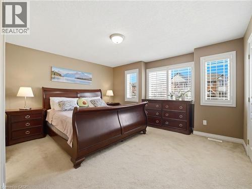 Carpeted room featuring multiple windows with white plantation shutters, neutral-toned walls, and a ceiling-mounted light fixture - 98 Willow Lane, Grimsby, ON - Indoor Photo Showing Bedroom