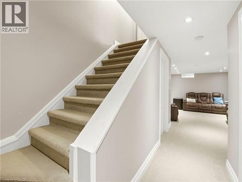 Carpeted staircase with white trim, leading to an expansive lower-level space featuring recessed lighting and neutral wall tones - 98 Willow Lane, Grimsby, ON - Indoor Photo Showing Other Room