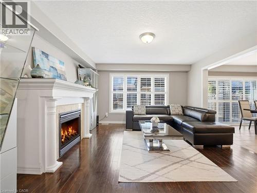 Living area featuring wood-finish flooring, a white mantel fireplace with a tile surround, and multiple windows with plantation shutters - 98 Willow Lane, Grimsby, ON - Indoor Photo Showing Living Room With Fireplace
