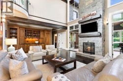 Expansive living area featuring a floor-to-ceiling stone fireplace, rich wood-finish flooring, built-in cabinetry with integrated lighting, and a two-story ceiling with exposed beams - 