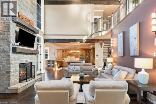 Two-story living area with a stone-clad fireplace and wood beam mantel - 253 Rossmore Boulevard, Burlington, ON - Indoor Photo Showing Living Room With Fireplace