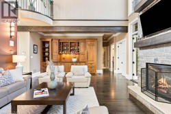 Hardwood flooring, stone-clad fireplace with hearth, built-in cabinetry, exposed wood beam, and an upper-level balcony with metal railings - 