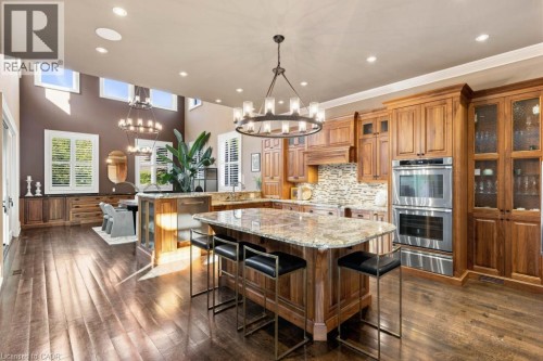 Kitchen featuring rich wood cabinetry, stainless steel double ovens, a large island with a stone countertop, and wood-finish flooring - 253 Rossmore Boulevard, Burlington, ON - Indoor