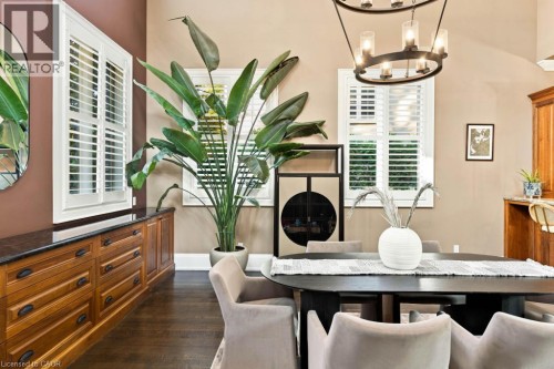 Built-in wood cabinetry with dark countertop, multiple windows with white plantation shutters, dark wood-finish flooring, and a contemporary chandelier - 253 Rossmore Boulevard, Burlington, ON - Indoor Photo Showing Dining Room