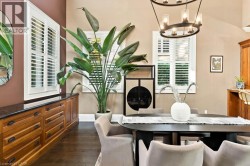 Built-in wood cabinetry with dark countertop, multiple windows with white plantation shutters, dark wood-finish flooring, and a contemporary chandelier - 
