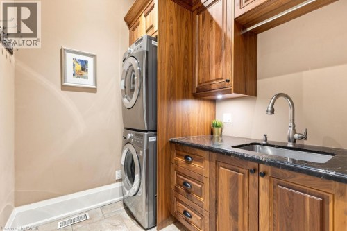 Laundry area featuring a stackable washer and dryer, wood-finish cabinetry, a sink with a gooseneck faucet, and a dark stone countertop - 253 Rossmore Boulevard, Burlington, ON - Indoor Photo Showing Laundry Room