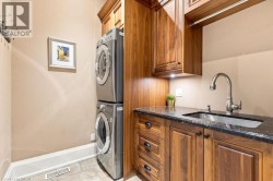 Laundry area featuring a stackable washer and dryer, wood-finish cabinetry, a sink with a gooseneck faucet, and a dark stone countertop - 