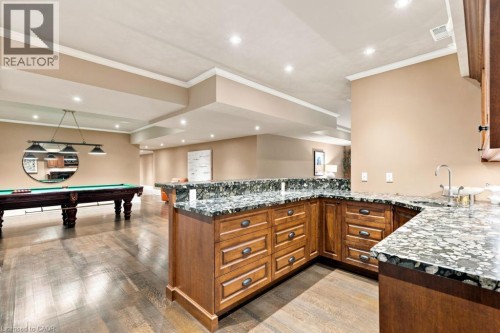 Spacious lower level featuring wood-finish flooring, recessed lighting, crown molding, and a wet bar with stone countertops and wood cabinetry - 253 Rossmore Boulevard, Burlington, ON - Indoor