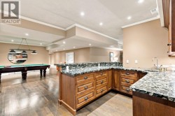Spacious lower level featuring wood-finish flooring, recessed lighting, crown molding, and a wet bar with stone countertops and wood cabinetry - 