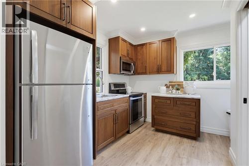 Renovated kitchen featuring warm wood cabinetry, stainless steel appliances including a refrigerator and electric range, white subway tile backsplash, wood-finish flooring, and abundant natural light - 21 Kerman Avenue, Grimsby, ON 