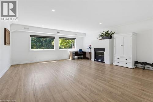 Bright, open living space featuring wood-finish flooring throughout, dual casement windows with natural light, built-in fireplace with surround, and white cabinetry with integrated storage - 21 Kerman Avenue, Grimsby, ON 