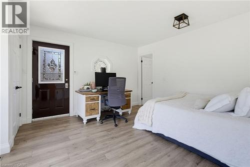 Bright bedroom with wood-finish flooring, abundant natural light from multiple windows, and a dedicated workspace featuring a desk with storage cabinetry and task seating - 21 Kerman Avenue, Grimsby, ON 