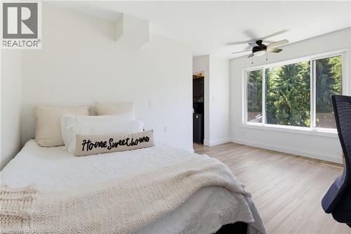 Bright primary bedroom showcasing light wood-finish flooring, large multi-panel windows with natural light, ceiling fan with integrated lighting, and neutral wall finishes - 21 Kerman Avenue, Grimsby, ON 