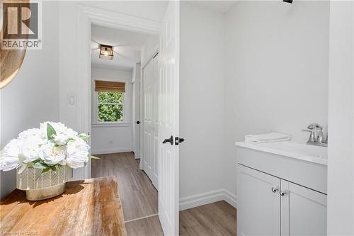 Bright hallway and powder room featuring wood-finish flooring, white painted walls, and soft-close cabinetry with polished chrome hardware - 21 Kerman Avenue, Grimsby, ON 
