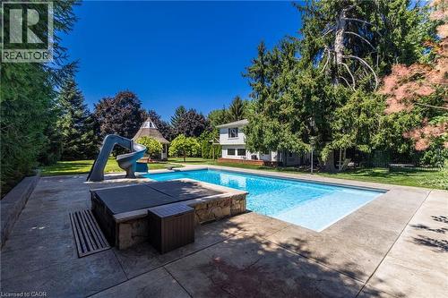 Resort-style backyard oasis featuring a sparkling in-ground swimming pool with sun lounging area, mature landscaping with privacy trees, modern patio hardscaping, and a two-story residence set on expa - 21 Kerman Avenue, Grimsby, ON 