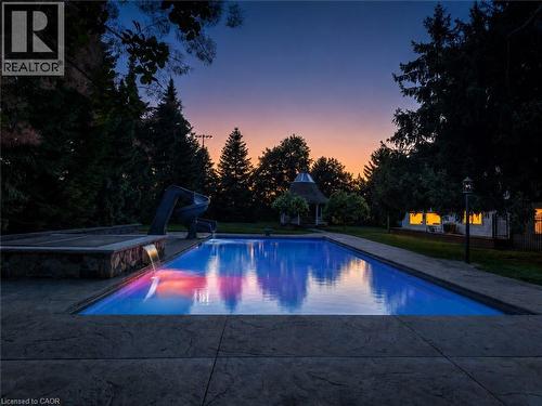Rectangular swimming pool with integrated slide, adjacent stone-clad water feature, and stamped concrete decking - 21 Kerman Avenue, Grimsby, ON 