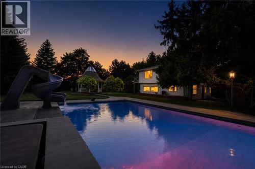 Expansive outdoor swimming pool with integrated slide, surrounded by a manicured lawn and mature trees - 21 Kerman Avenue, Grimsby, ON 