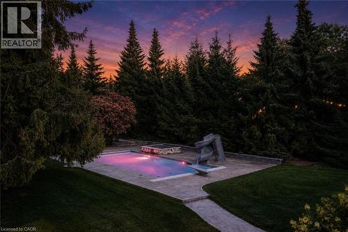 Swimming pool with integrated slide, surrounded by a stone patio and manicured lawn - 21 Kerman Avenue, Grimsby, ON 