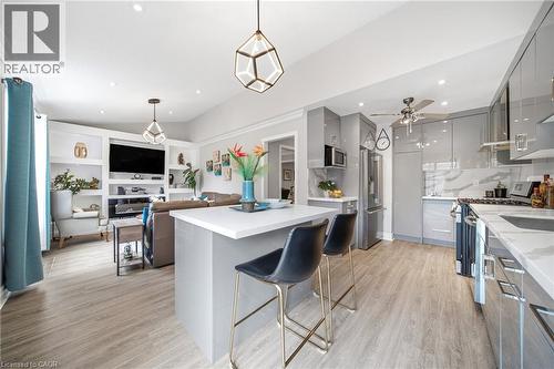 Open-concept living area featuring wood-finish flooring, a kitchen island with seating, glossy gray cabinetry, stainless steel appliances, and built-in shelving in the living space - 5184 Red Brush Drive, Mississauga, ON - Indoor Photo Showing Kitchen With Upgraded Kitchen