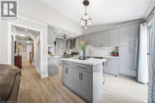 Modern kitchen featuring a central island with a light-toned countertop, sleek gray cabinetry, a white stone-finish backsplash, stainless steel appliances, and wood-finish flooring - 5184 Red Brush Drive, Mississauga, ON - Indoor Photo Showing Kitchen