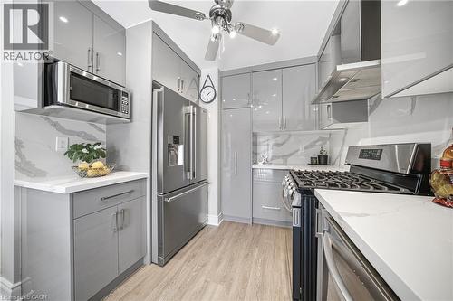 Galley kitchen featuring light gray high-gloss cabinetry, stainless steel appliances, white countertops, and wood-finish flooring - 5184 Red Brush Drive, Mississauga, ON - Indoor Photo Showing Kitchen With Stainless Steel Kitchen With Upgraded Kitchen