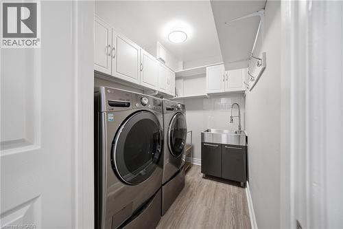 Dedicated laundry room featuring light wood-finish flooring, white cabinetry, and a utility sink with a high-arc faucet - 5184 Red Brush Drive, Mississauga, ON - Indoor Photo Showing Laundry Room
