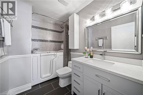 Bathroom featuring a walk-in tub, a single vanity with a white countertop, a mirrored vanity light fixture, a wall-mounted cabinet, and large-format floor tiles - 5184 Red Brush Drive, Mississauga, ON - Indoor