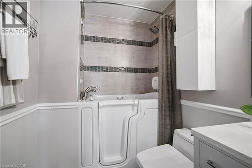 Bathroom featuring a walk-in tub with chrome fixtures, tiled shower surround with accent banding, and a wall-mounted storage cabinet - 5184 Red Brush Drive, Mississauga, ON - Indoor Photo Showing Laundry Room